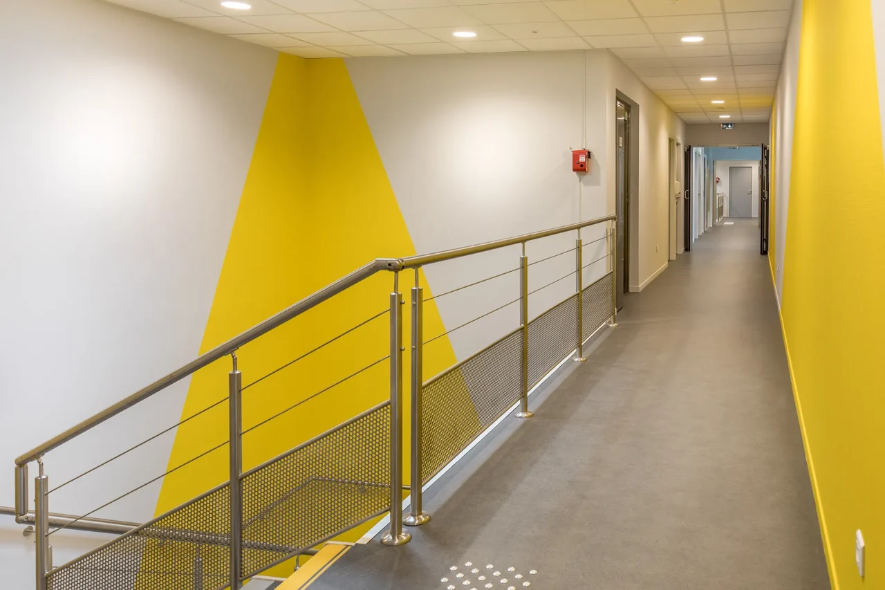 Couloir intérieur de bureaux avec garde-corps métallique et mur graphique jaune sur site industriel
